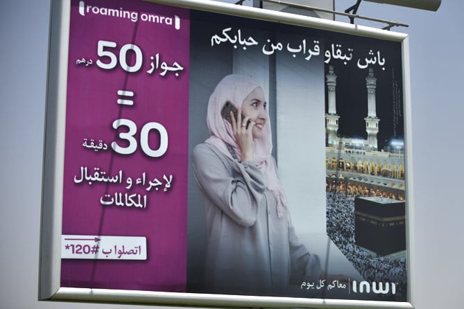 billboard with a picture of a woman in a hijab making a mobile call with Mecca as a backdrop