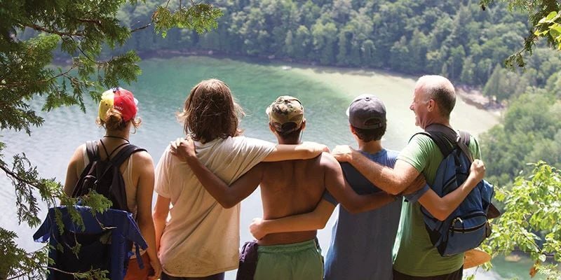 Group from Rock Point School with their arms around one another overlooking a forested lake from a scenic overlook, representing friendship, belonging, outdoor learning, and the supportive community fostered through shared experiences.