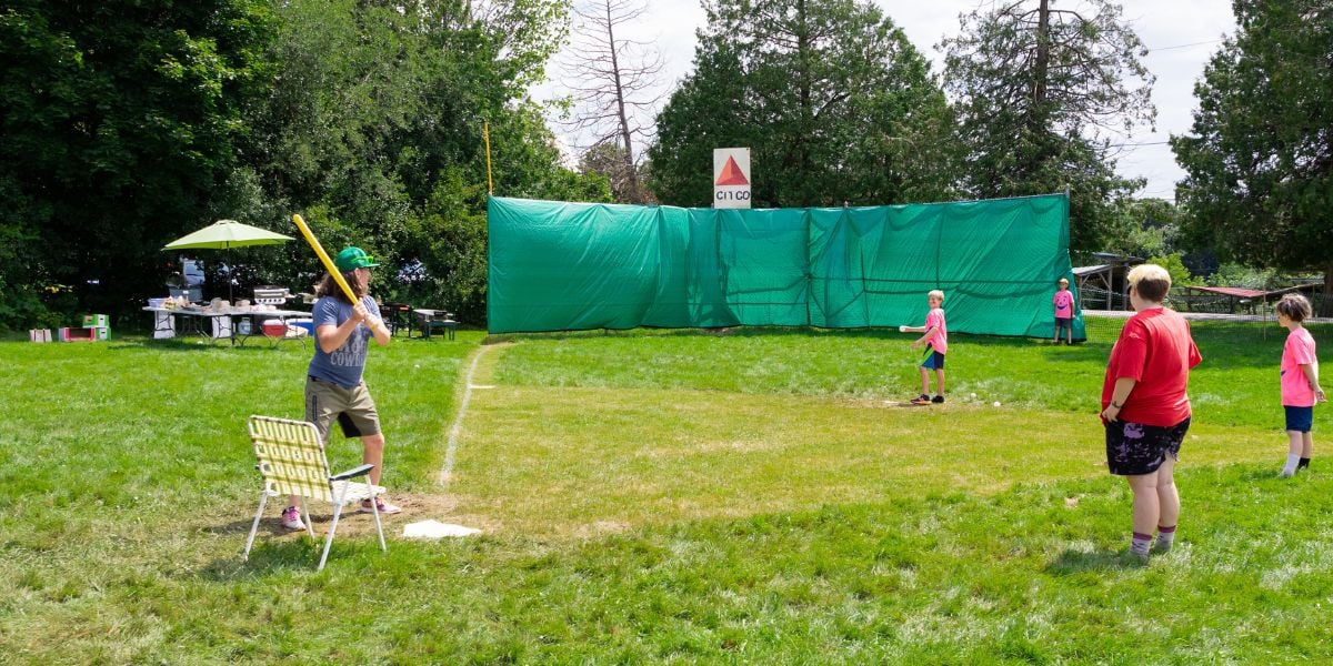 A wiffle ball game is in progress, the pitcher in a pink tshirt about to throw to a batter standing ready at the plate on at Rock Point School